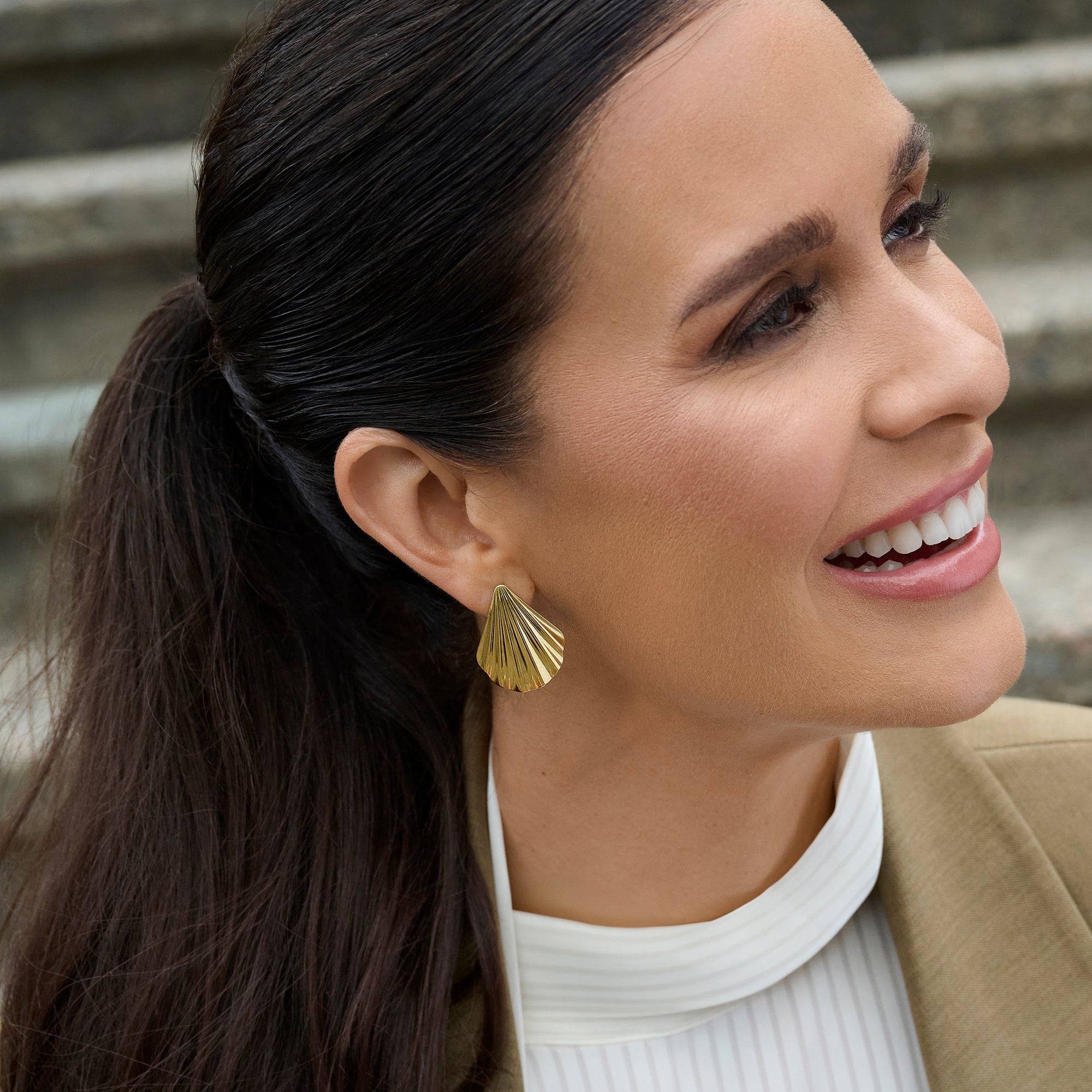 Gold stainless steel shell-inspired stud earrings worn on ear, bold sculptural jewelry design, hypoallergenic non-tarnish durable earrings, elegant modern statement jewelry.
