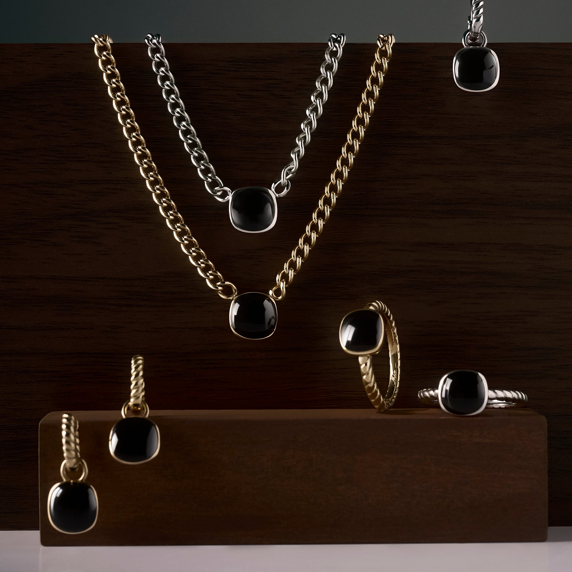 Black gemstone jewelry collection with gold and silver stainless steel pendant necklaces, drop earrings and twisted band rings, bold modern statement pieces with polished black stones.