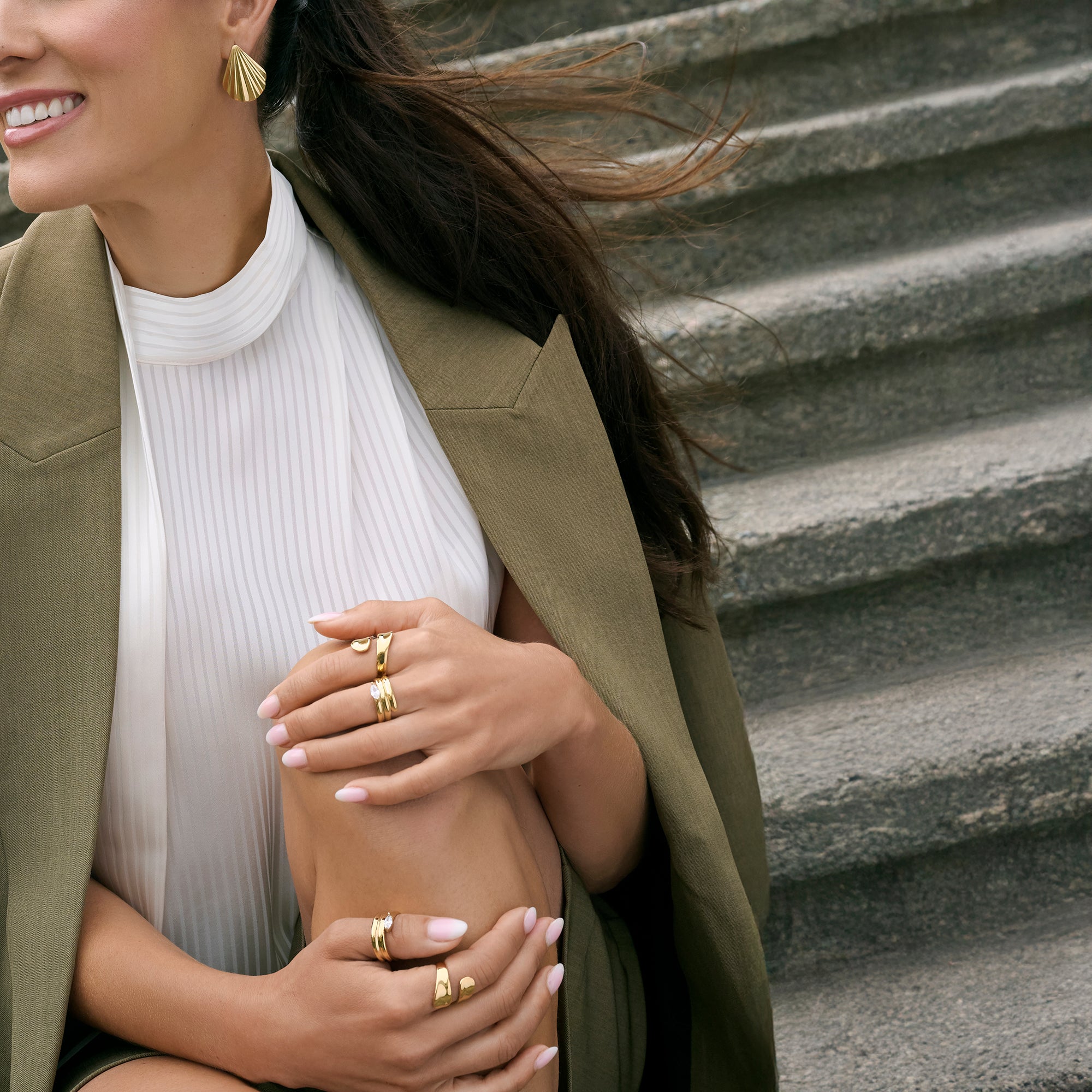 Gold stainless steel shell stud earrings with stacked minimalist rings worn on hand, modern sculptural jewelry styling, hypoallergenic non-tarnish durable everyday jewelry, elegant contemporary fashion jewelry.
