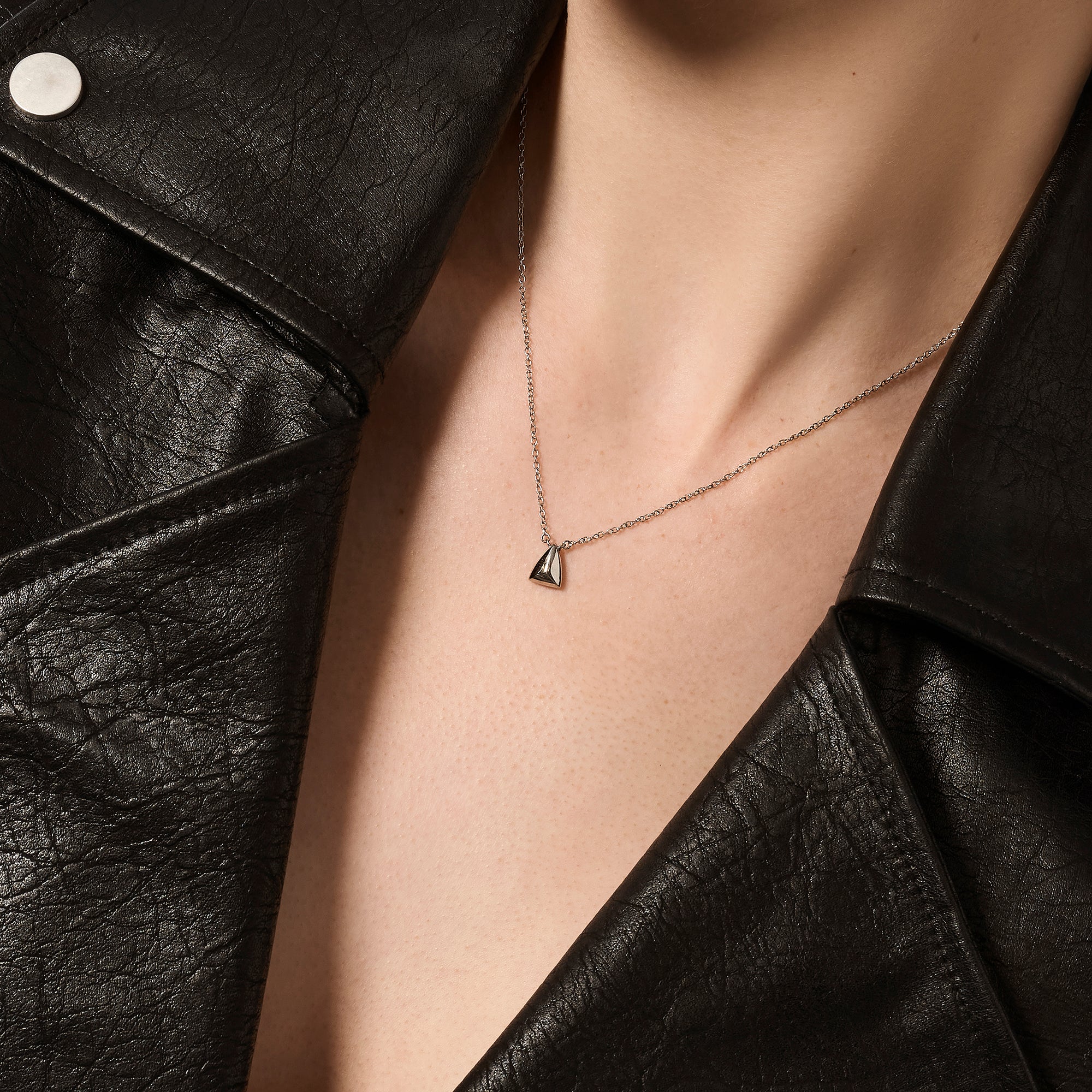 Silver stainless steel geometric pendant necklace worn on neckline with triangular charm, minimalist modern jewelry, hypoallergenic non-tarnish durable everyday necklace, sleek contemporary jewelry design.
