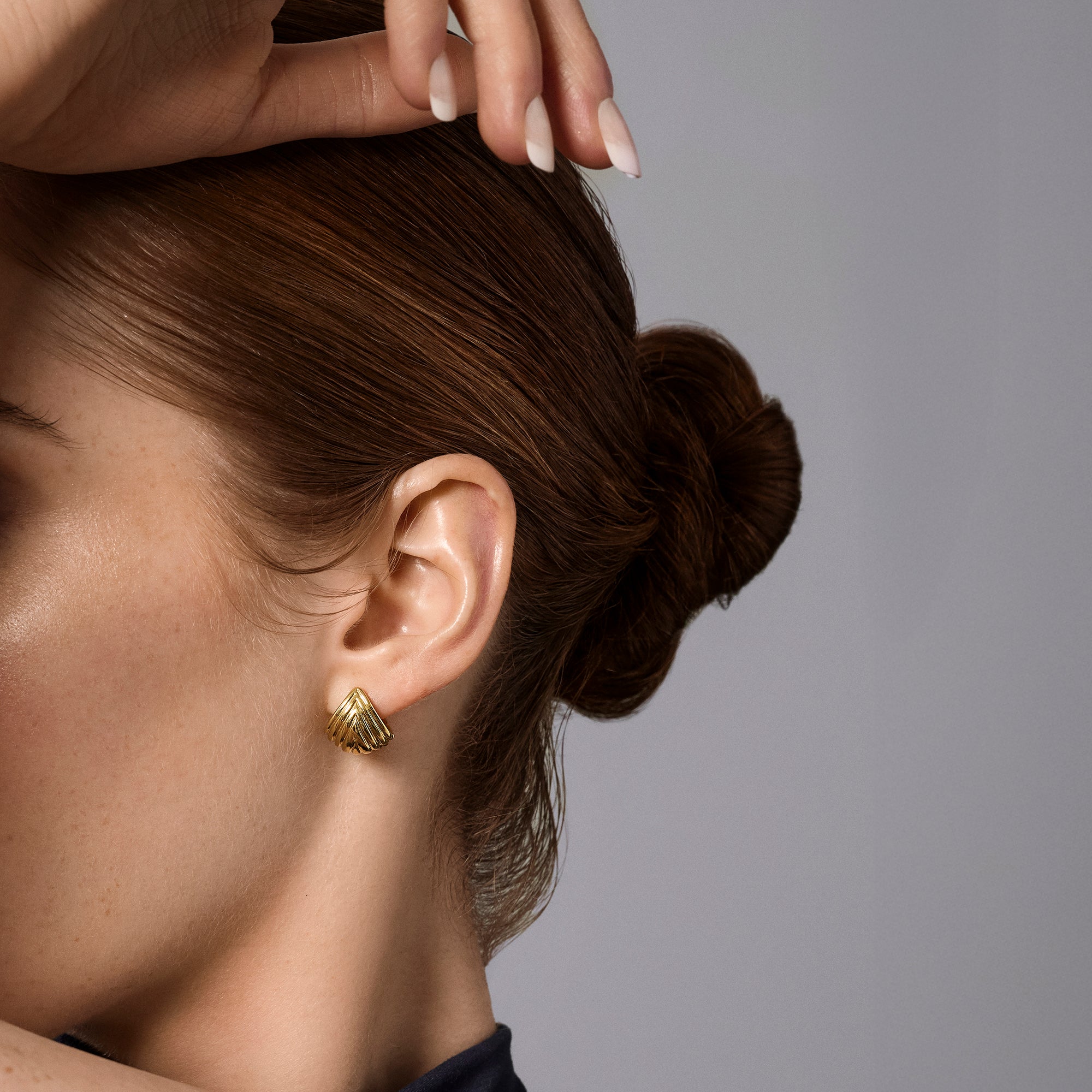 Gold stainless steel sculptural fan-shaped stud earrings worn on ear, layered geometric jewelry design, hypoallergenic non-tarnish durable earrings, elegant contemporary statement jewelry.
